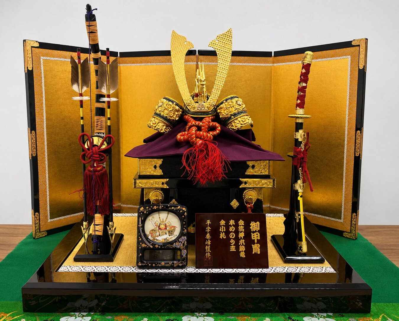 金屏風を背景に飾られた五月人形。黒漆塗りの台に金色の装飾を施した兜を中心に、矢羽根と太刀を左右に配した買取品